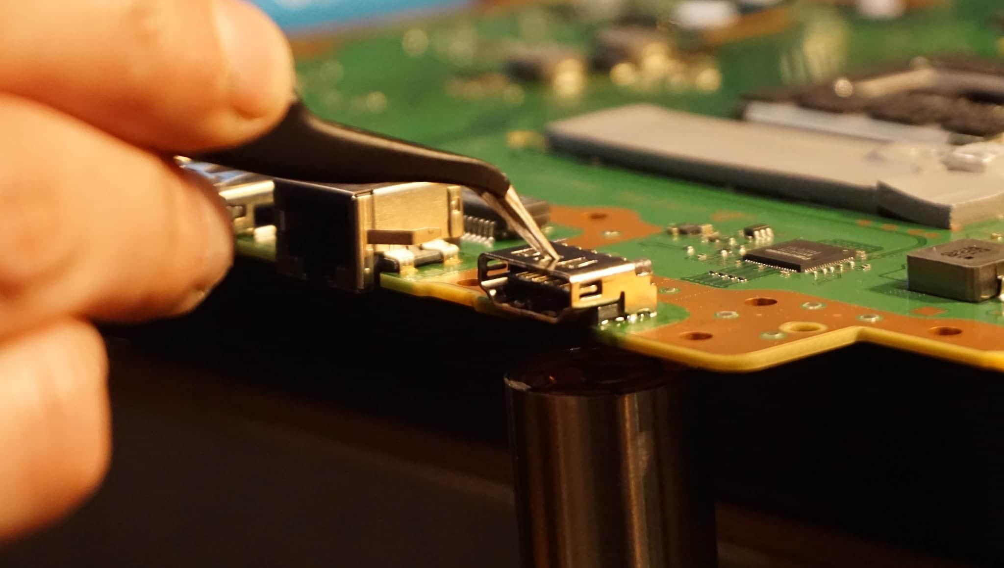 Console HDMI port repair work with precision tweezers