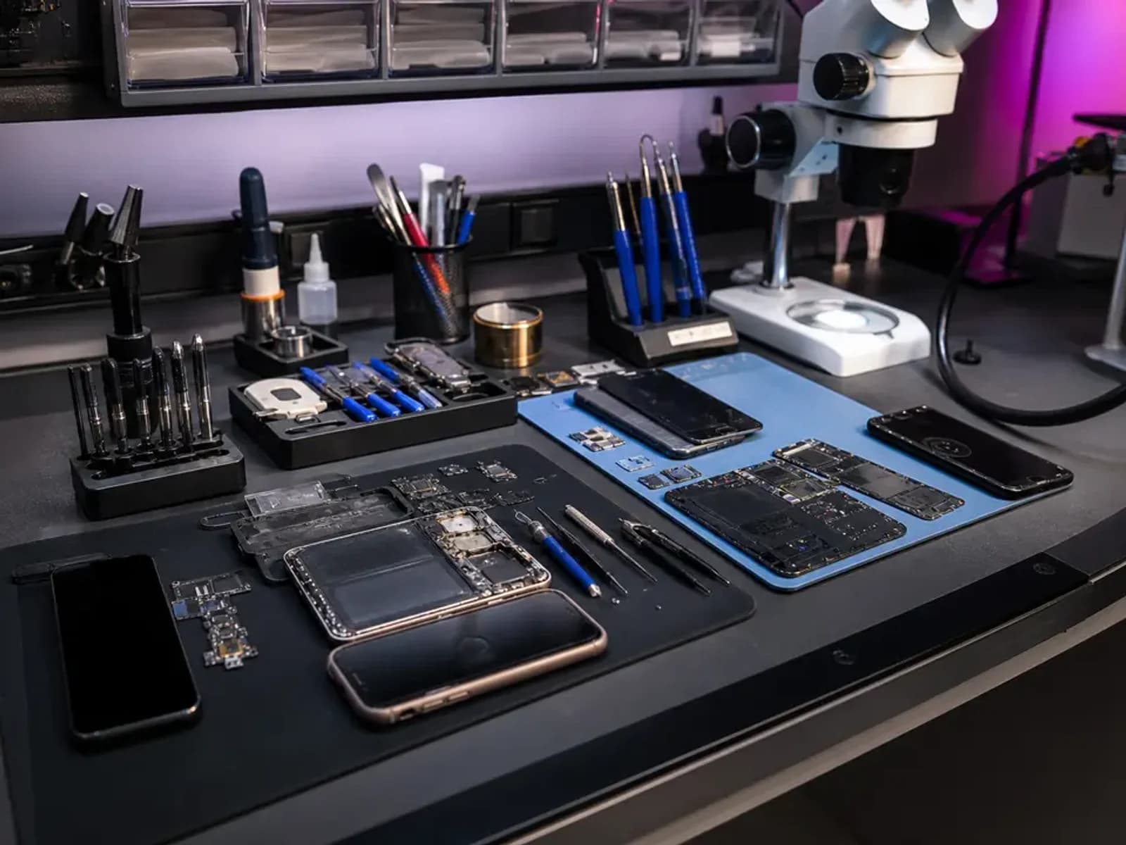 Cell phone repair workbench with smartphones, precision tools, and a microscope